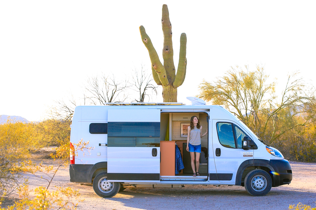 Wondering how to insure a self-built campervan? You're in the right place! Image of a woman in the desert looking out of a camper van.