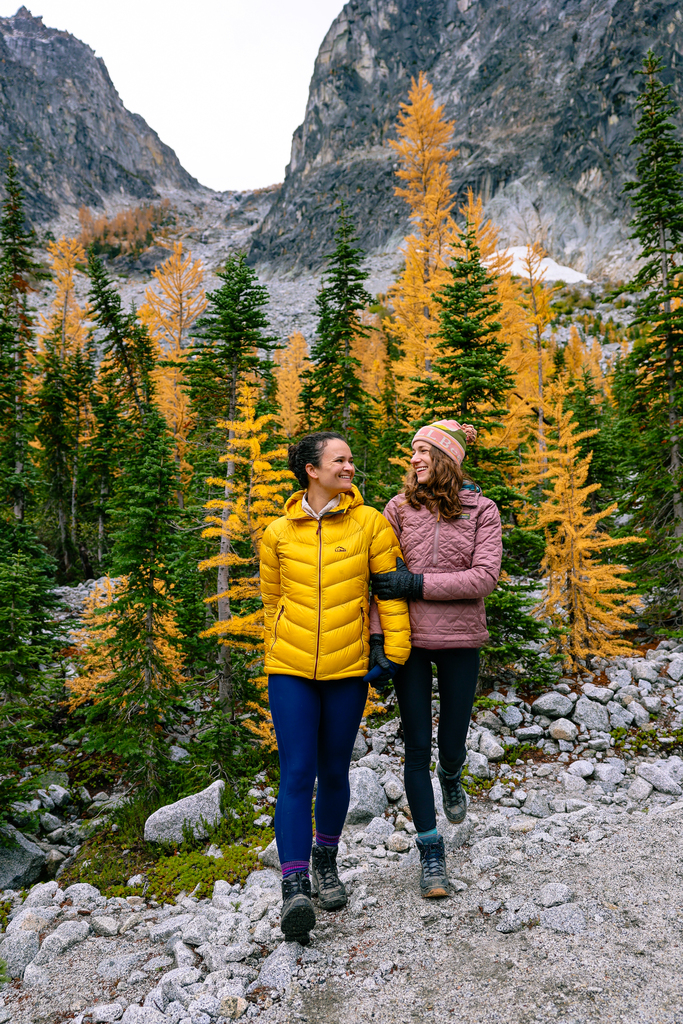 Gwyn and Ami amongst the larches in the enchantments in washington state. Gwyn and Ami are an LGBTQ+ couple that creates travel, hiking, and outdoor adventure content.