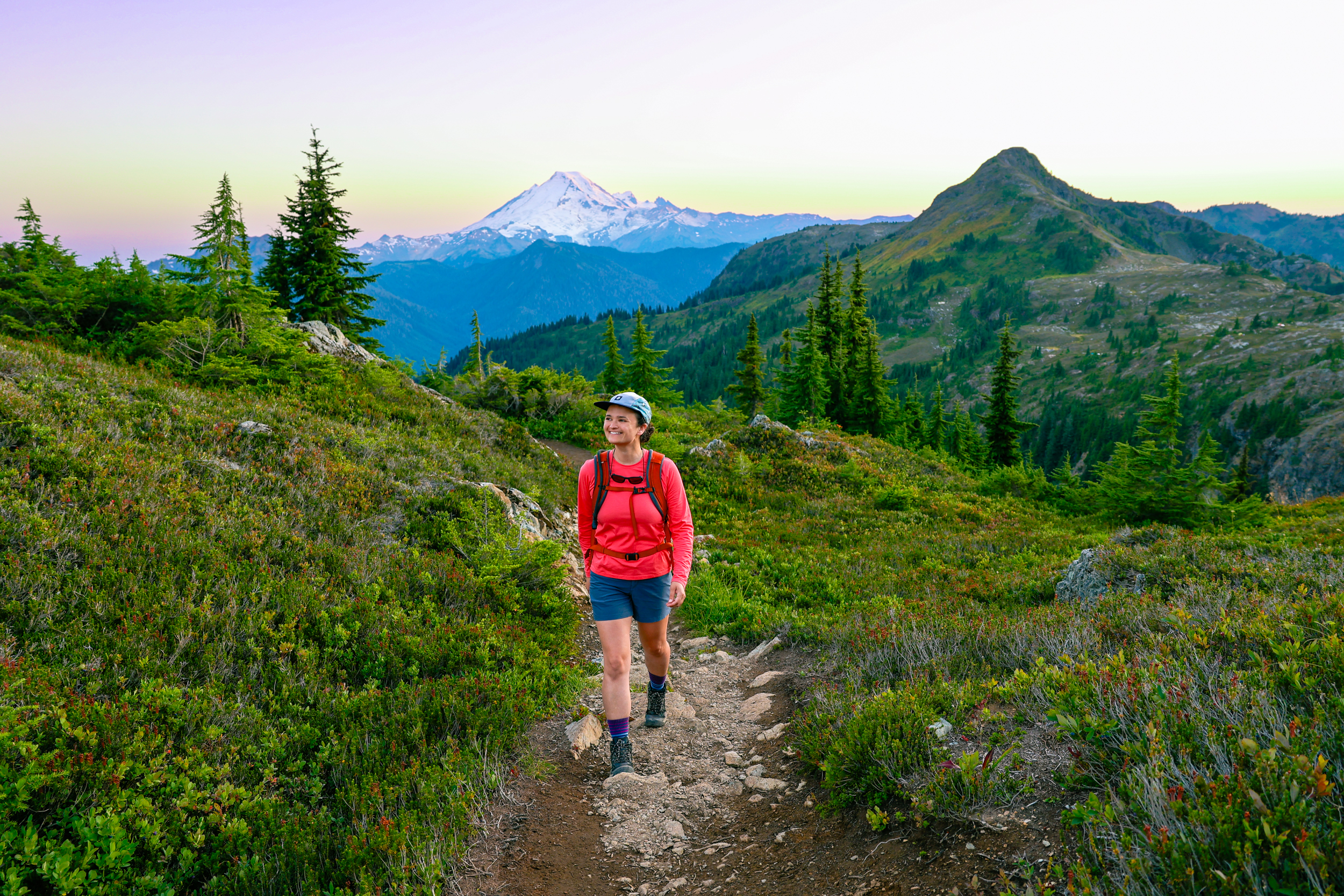 Woman hiking along the yellow aster butte trail with views of mount baker at sunset in the background