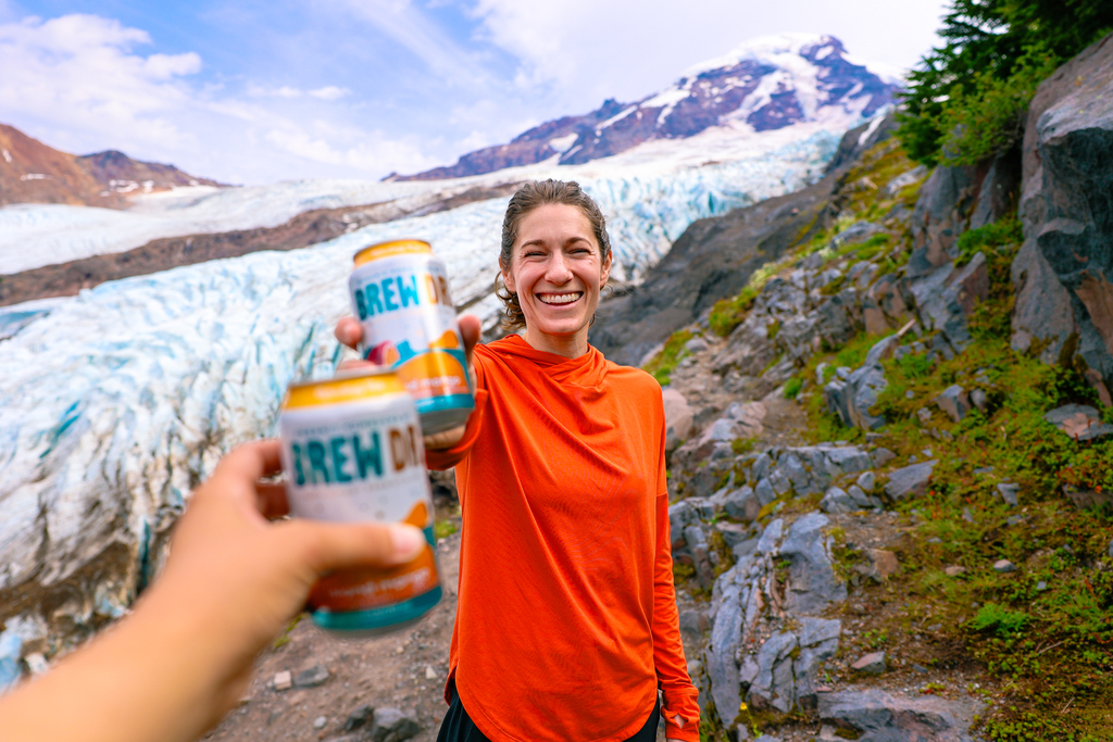 Woman wearing the REI Co-op Sahara Shade Hoodie in Washington on the Heliotrope glacier hike while enjoying a Brew Dr kombucha