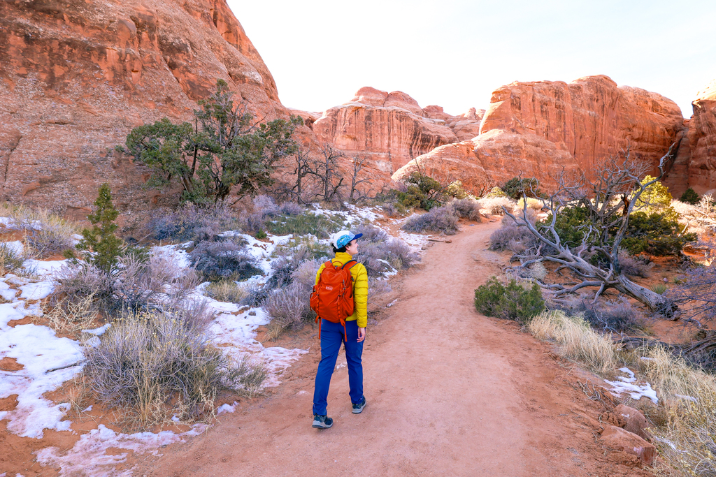 Woman hiking in Arches national park in winter. Comfortable hiking pants, base layers, and warm jackets are amongst the items to pack for a winter trip to Arches National Park