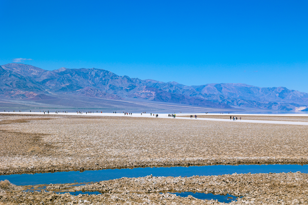 Badwater basin in Death Valley National Park, California USA. People pictured walking out to the salt flats and lake.