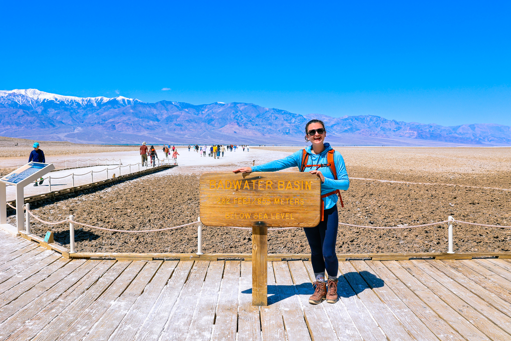 Woman standing oj the boardwalk with the sign at Badwater basin in Death Valley National Park, California USA. This is the lowest point in north America.