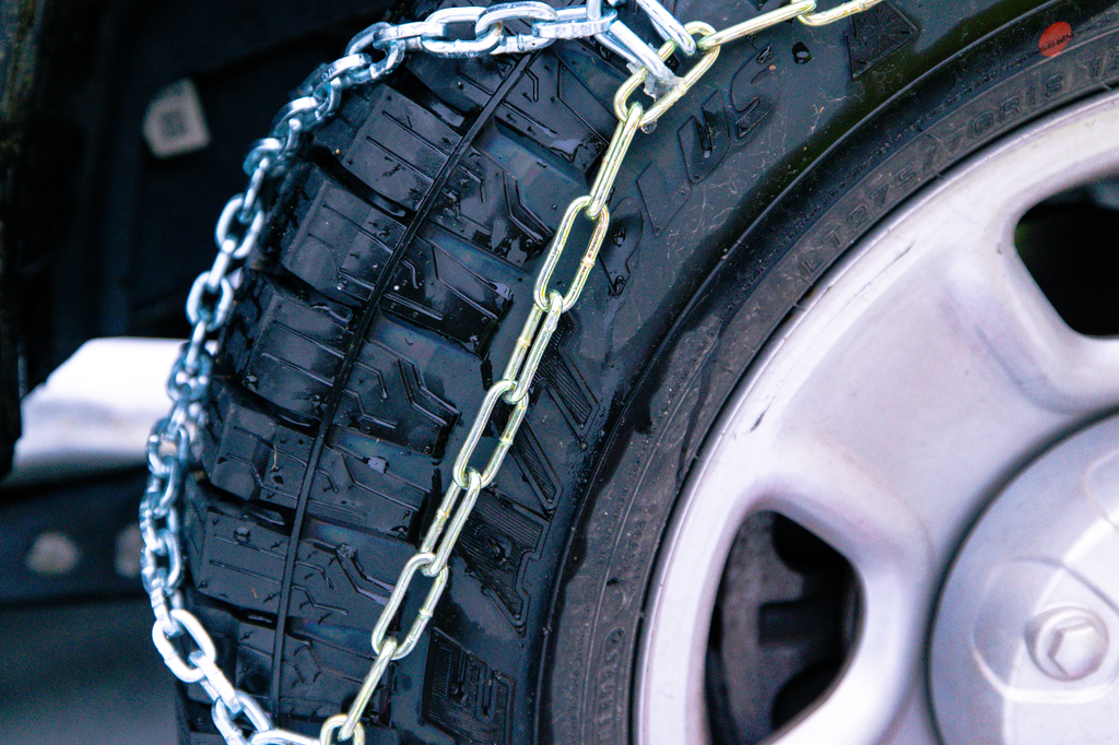A close up picture of a Les Schwab Open Range A/T Plus tire with a tire chain installed on it.